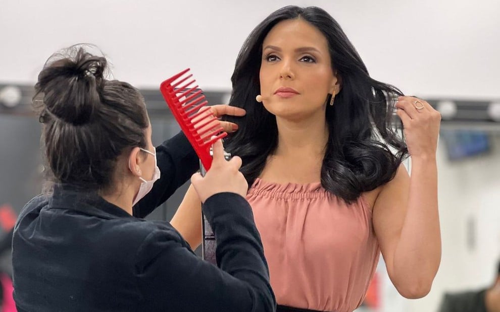 Uma mulher está de costas e segura um pente vermelho; Márcia Dantas está de frente para ela e mexe nos cabelos