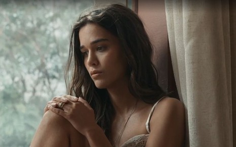 Em cena de Renascer, Theresa Fonseca está sentada em uma janela, pensativa; ela está com as mãos no joelho