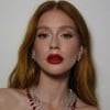 Marina Ruy Barbosa está maquiada e usa um batom vermelho escuro, da mesma cor das pedras de um colar; ela encara a câmera