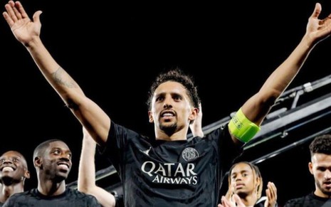 Marquinhos de braços abertos para o alto comemorando vitória do PSG na Champions League; ele usa uniforme preto