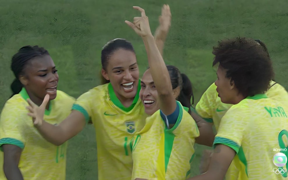 Marta no centro levanta as mãos para o alto e é abraçada por colegas da Seleção Brasileira