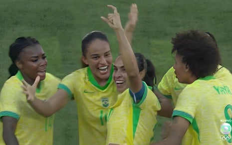 Marta no centro levanta as mãos para o alto e é abraçada por colegas da Seleção Brasileira