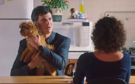 O ator Mateus Solano como Jonas segurando um cachorro caramelo no colo em cena de Elas por Elas