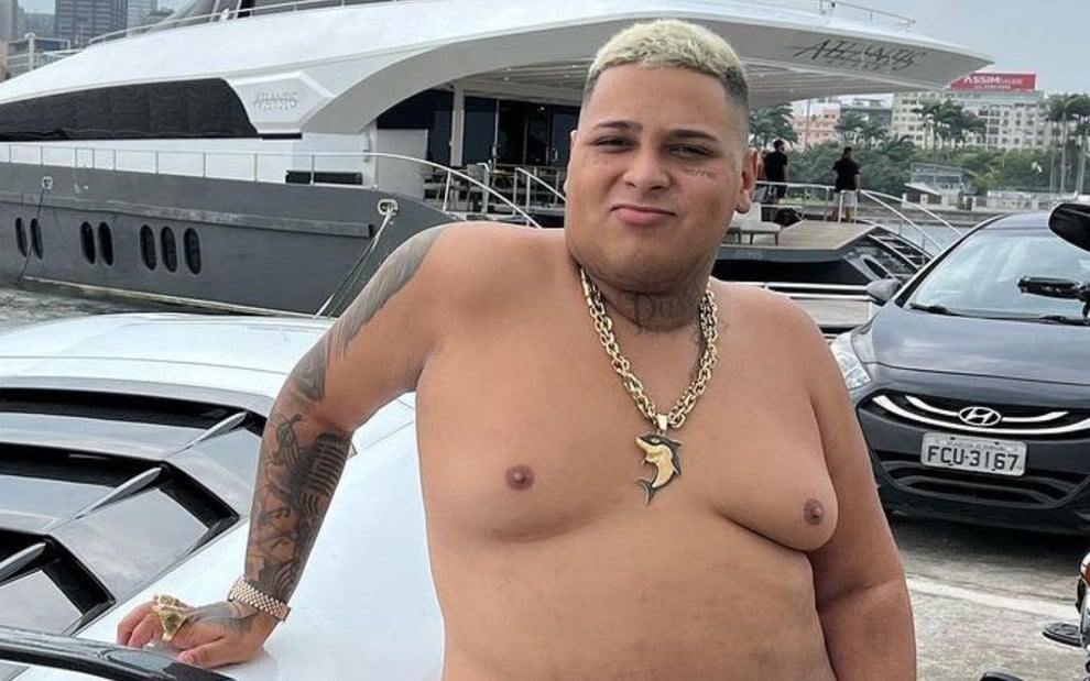 MC Ryan está sem camisa e se apoia em um iate