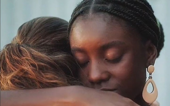 Em cena de Terra e Paixão, Renata Gaspar está de costas, abraçada a Camilla Damião, que está de olhos fechados
