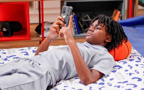 Romeu (Miguel Ângelo) deitado na cama e olhando o celular
