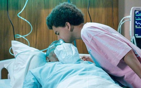 Téo (Miguel Schmid) beija a testa de Leandro (Guilherme Sant'Anna), que está deitado em cama de hospital