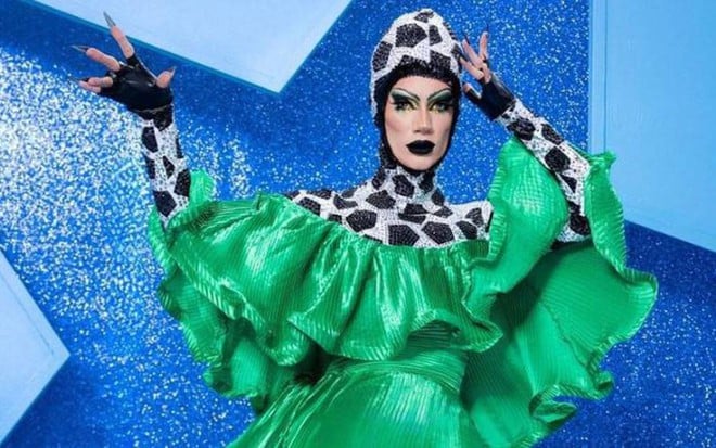 Vestida de bola de futebol, a drag queen Miranda Lebrão está na frente de um fundo azul com uma estrela