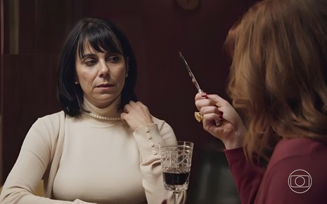 A atriz Paula Cohen com mão na gola da blusa, em frente à atriz Isabel Teixeira com faca na mão, em cena de Elas por Elas