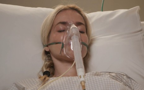 Monique Alfradique está deitada em cama de hospital e usando oxigênio em cena da novela Elas por Elas
