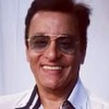 O cantor Nahim usa uma camisa branca e um óculos escuro; ele sorri para a câmera
