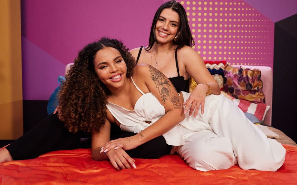 Fernanda Bande e Giovanna Pitel estão recostadas uma na outra em uma cama vermelha com fundo cor-de-rosa