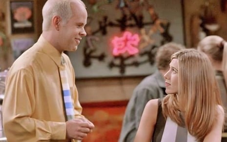 James Michael Tyler olha sorridente para Jennifer Aniston em cena de Friends