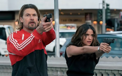 Nick Zano e Shelley Hennig apontam armas em cena da série Explosivos