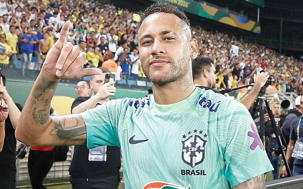 Neymar está com a camisa da Seleção Brasileira e faz hang loose com a mão