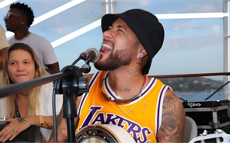 Neymar cantando e tocando, com uma camiseta dos Lakers e chapéu preto