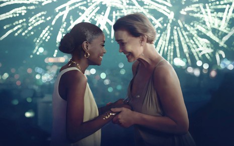 Jennifer Dias e Júlia Lemmertz em cena da série No Ano que Vem, de mãos dadas, em frente a paisagem noturna com fogos de artifício