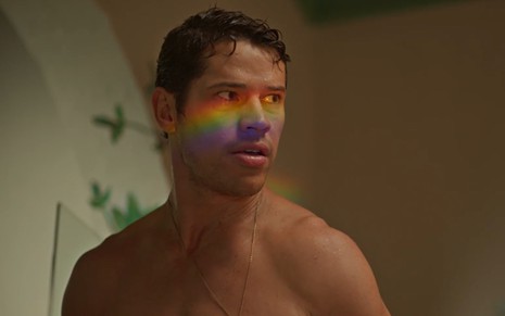 O ator José Loreto sem camisa, com cores do arco-íris na região dos olhos, em cena de No Rancho Fundo