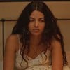 A atriz Larissa Bocchino caracterizada como Quinota em No Rancho Fundo, com expressão séria, sentada em cama