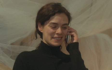 Bahar (Özge Özpirinçci) está no celular e sorri em cena da novela Força de Mulher