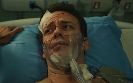 Pablo Sanábio está deitado em maca bastante machucado e usa oxigênio em cena da série Sob Pressão