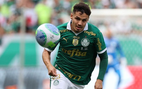 Imagem colorida mostra o jogador Rafael Veiga, do Palmeiras, vestido com o uniforme verde, em meio ao campo de futebol e chutando uma bola