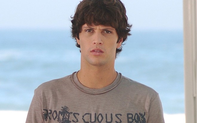 O ator Gustavo Leão com expressão séria em cena de Paraíso Tropical, com céu azul no plano de fundo
