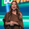 Patricia Abravanel sorridente no quadro Show do Milhão; ela está de cabelos soltos e usa vestido marrom