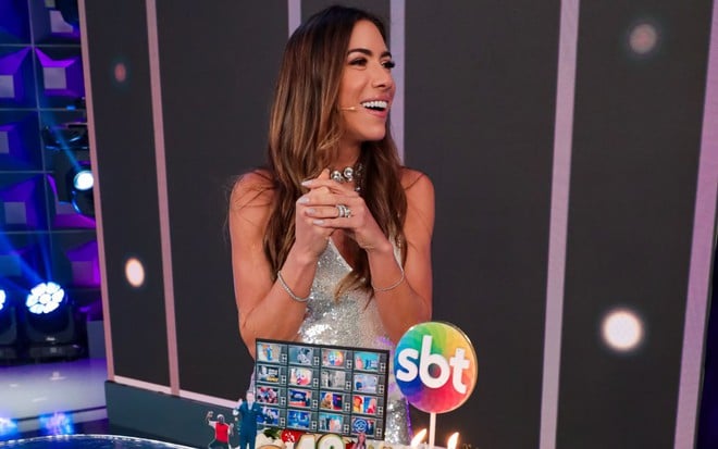 Patricia Abravanel olha para o lado e bate palmas; há um bolo na frente dela em comemoração aos 43 anos do SBT