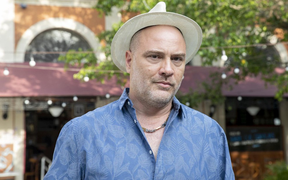 Paulo Tiefenthaler posa de chapéu e blusa azul e branca no cenário de Travessia