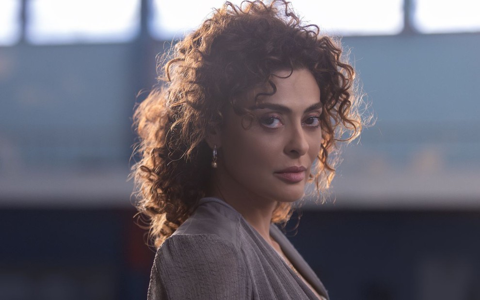 A atriz Juliana Paes olhando para a câmera, com cabelo cacheado preso, caracterizada como sua personagem em Pedaço de Mim, série da Netflix