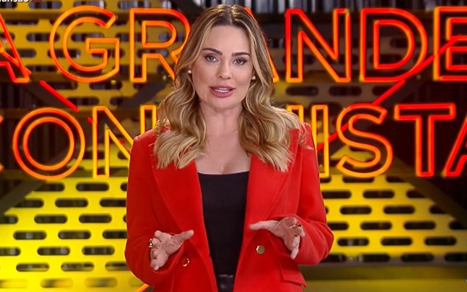 Rachel Sheherazade usa um blazer vermelho e gesticula em A Grande Conquista 2