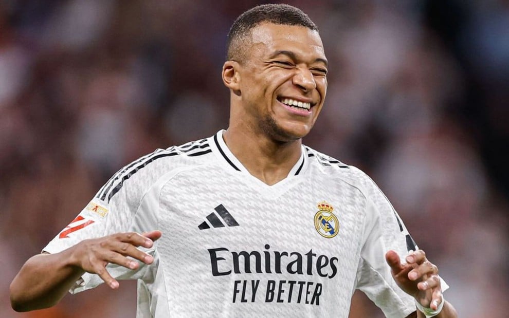 Mbappé, do Real Madrid, veste uniforme branco com detalhes em preto e sorri durante partida