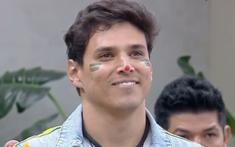 Bruno Cardoso com uma pintura facial de dois riscos verdes em cada bochecha em cena de A Grande Conquista