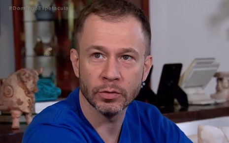 O jornalista Tiago Leifert usa camiseta azul e olha para cima em entrevista à Record