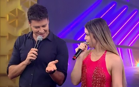 Rodrigo Faro sorri nervosamente ao lado de Melody, que tem expressão tranquila no palco do Hora do Faro