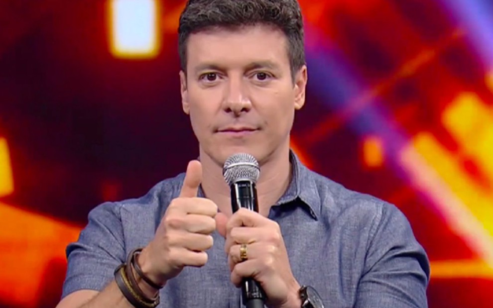 Rodrigo Faro faz um sinal de joia com a mão esquerda no programa Hora do Faro