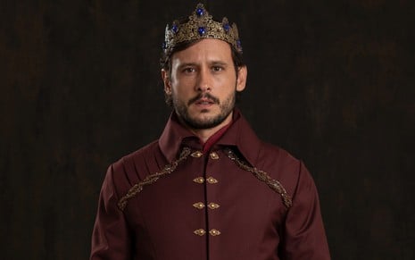 Guilherme Dellorto posa com casaco bordô e uma coroa na cabeça em foto promocional de Reis