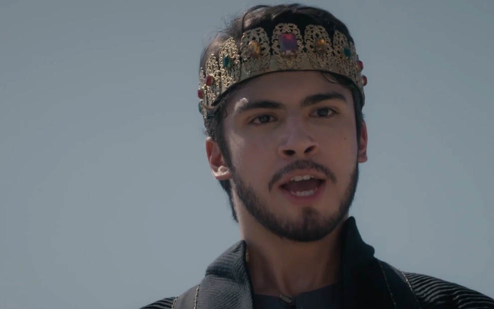 Henrique Camargo tem expressão imponente e uma coroa na cabeça em cena de Reis