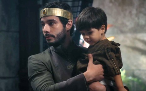 Vitor Novello com uma criança no colo como o seu filho Abias interpretando Jeroboão na novela Reis