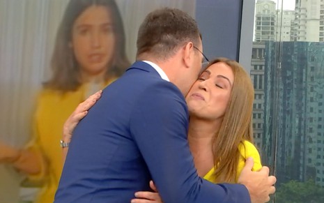 Rodrigo Bocardi abraça Ananda Apple no cenário do Bom Dia São Paulo; no telão há uma foto da repórter mais jovem