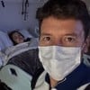 Rodrigo Faro usa máscara e está na frente de um leito hospitalar, no qual Vera Viel está deitada