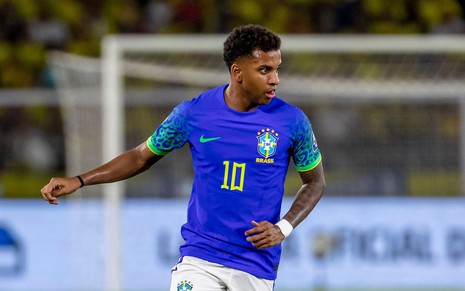 Rodrygo usa camisa 10 da Seleção Brasileira com uniforme azul e branco; ele está fazendo movimento de correr com a bola