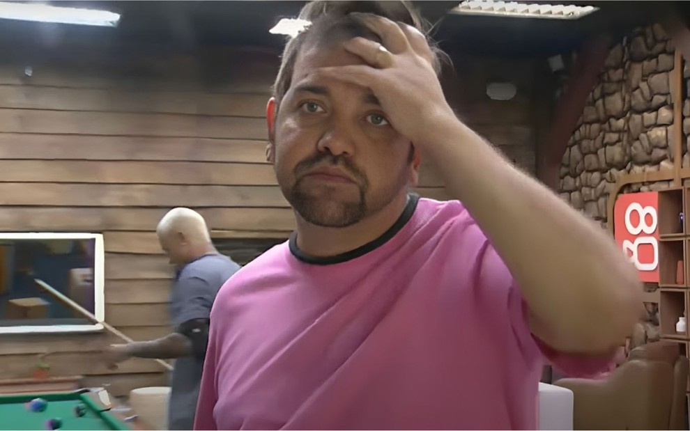 Sander Mecca com a mão no rosto, usando camisa rosa