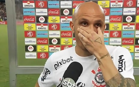 Fábio Santos tenta segurar as lágrimas com a mão no rosto em entrevista ao SBT