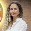 Luciana Valério posa diante de uma parede de vidro com logo do SBT ao fundo