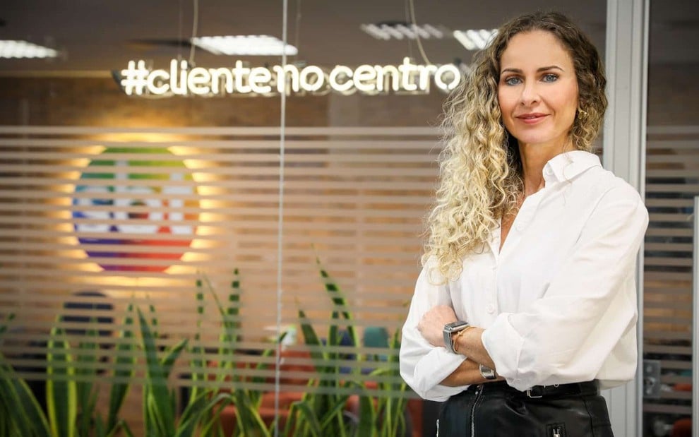 Luciana Valério posa diante de uma parede de vidro com logo do SBT ao fundo