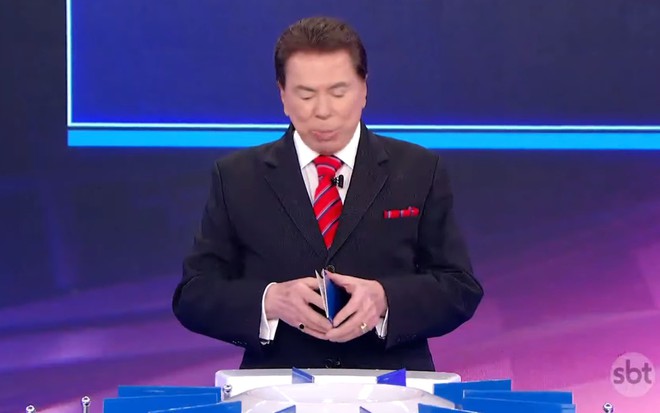 Silvio Santos está cabisbaixo e espia papel no Jogo das 3 Pistas do Programa Silvio Santos