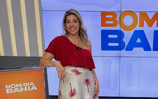 A apresentadora Silvana Freire posa no cenário do telejornal Bom Dia Bahia, da TV Aratu; ela está com blusa vermelha e saia florida