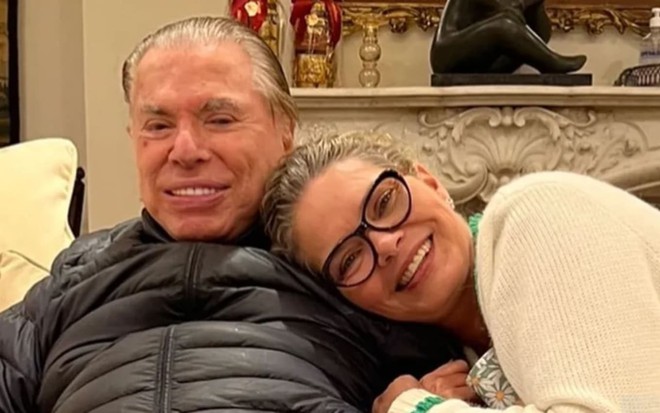 Cintia Abravanel está apoiada num ombro do pai, Silvio Santos, e sorri para a câmera